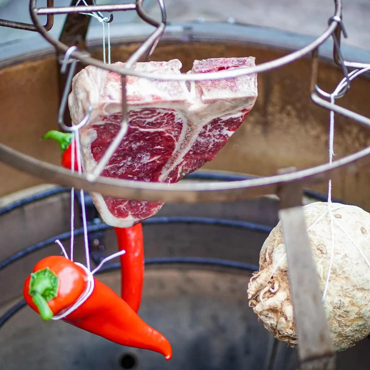 Chilischoten, ein Steak und eine Sellerieknolle hängen zum Räuchern am MONOLITH Smoke Set